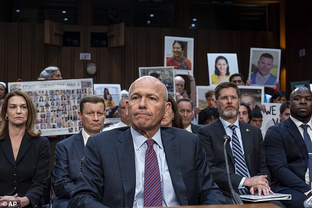 Boeing CEO Dave Calhoun takes his seat to testify before the Senate Homeland Security and Governmental Affairs Investigations Subcommittee with protesters in the hearing.