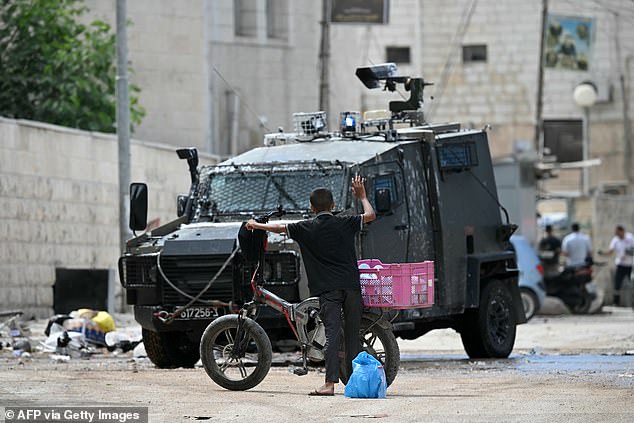 A Palestinian boy raises his arm in the air as Israeli soldiers inspect what he is carrying during a raid in Jenin.