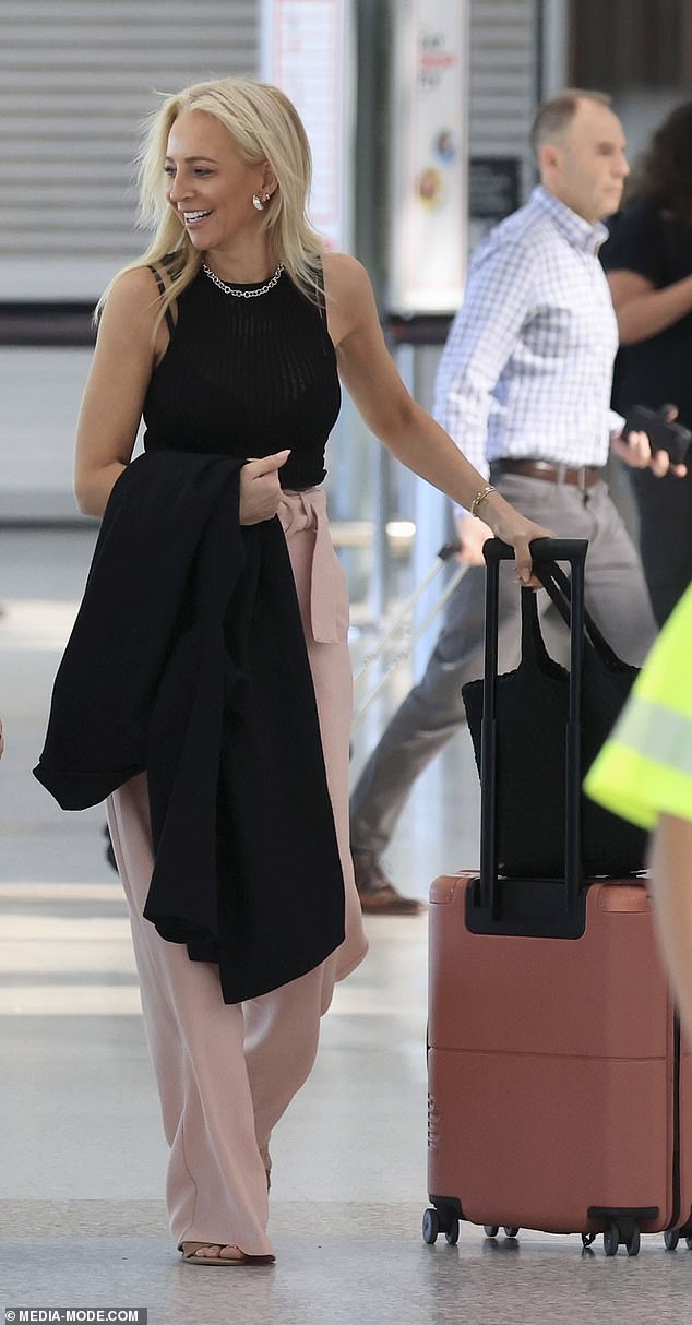 She also accessorized her look with a shiny silver necklace with large links and matching silver earrings while carrying her pink carry-on luggage.