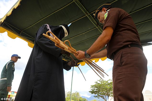 An officer holds a bundle of stiff wooden batons, which he is later seen handing to a thief.