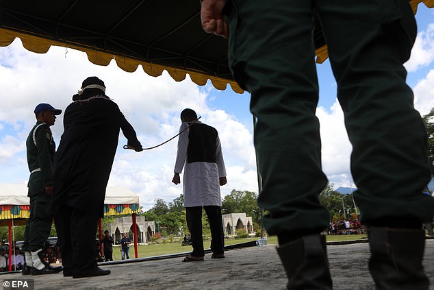 Officers watch as a man, seen clenching his fists, is whipped with a rod in Indonesia