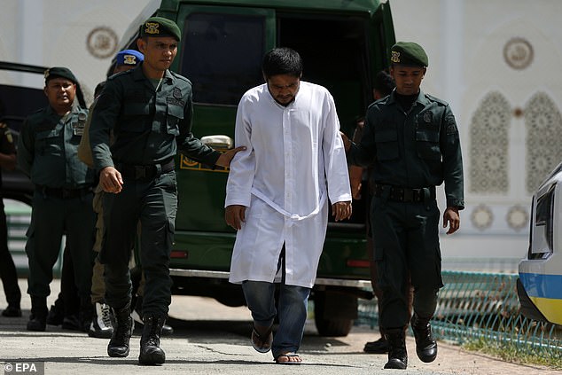 A man who is about to receive a public beating for violating Sharia law is escorted away by Sharia police in Jantho