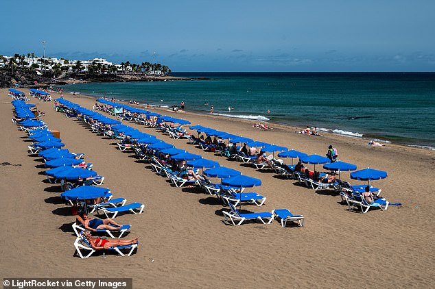 Tourists sunbathe, swim and relax on Playa Grande in Puerto del Carmen, located in the southeast of the volcanic island of Lanzarote.