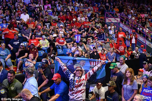 A man holds a flag as another man is detained by security and police after jumping onto the media platform at a campaign rally for the Republican presidential candidate.