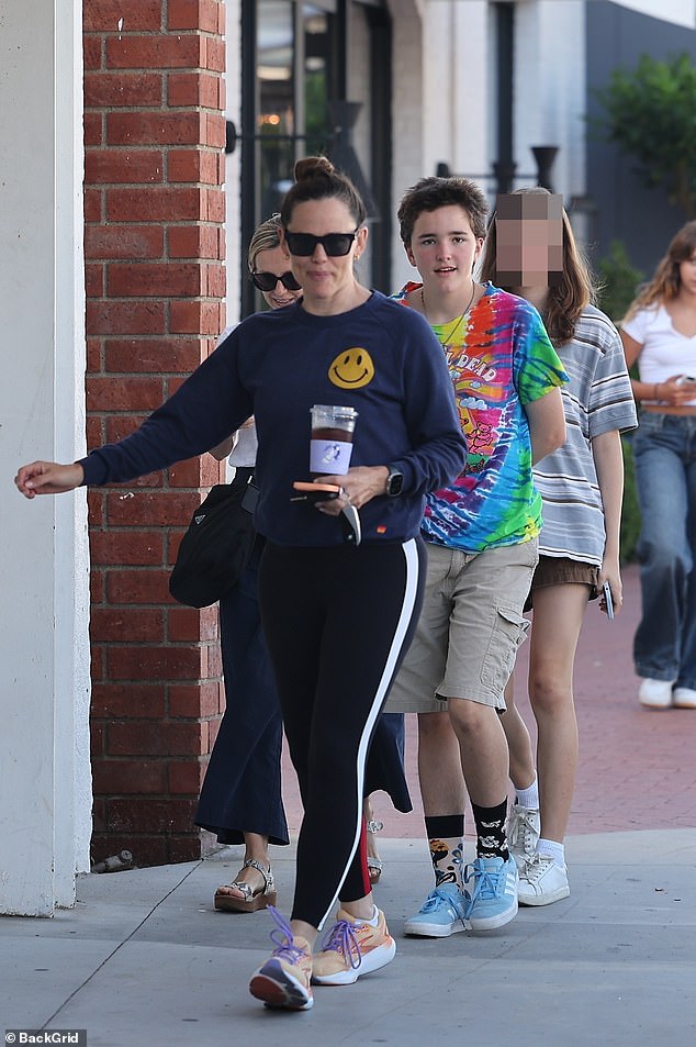 For her laid-back outing, the 52-year-old actress wore a navy blue long-sleeved shirt with a yellow smiley face, black leggings with white racing stripes down each leg, and beige sneakers with purple laces.