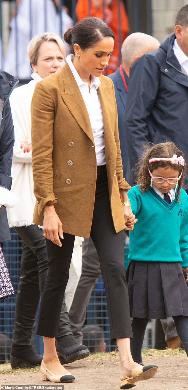 Meghan looked sophisticated in high-waisted black skinny jeans, which she paired with a white button-down business shirt with one button on the top left undone, tucked in.