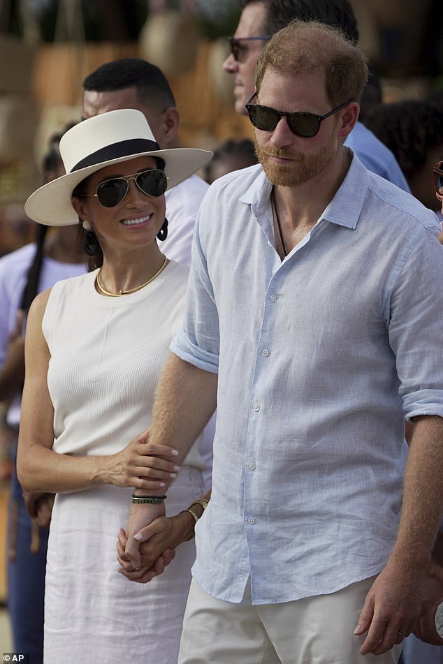 Meghan holds Harry's arm as they walk through the anti-colonial village of San Basilio de Palenque in Colombia.