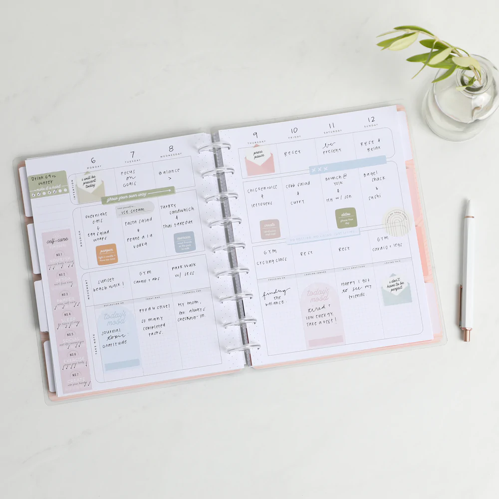 Open happy planner with notes taken next to a pen and a plant