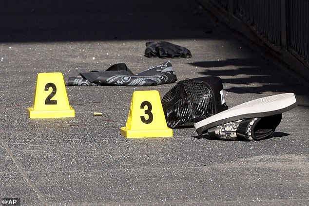 Blood and a bullet casing labeled as evidence are seen as police officers secure the area.