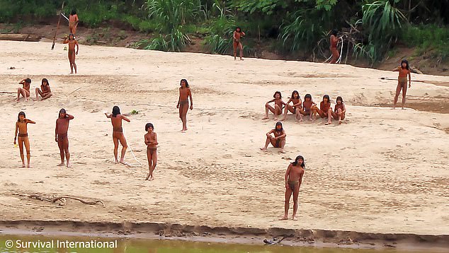 Tribe members rest on the riverbanks while others carry spears and stop to interact (pictured, June)