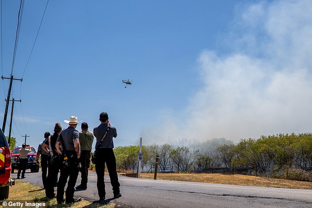 Members of the Hays County Emergency Services Districts and Kyle and Buda Fire Departments watch as a helicopter prepares to drop water on a wildfire during an excessive heat warning in August 2023.