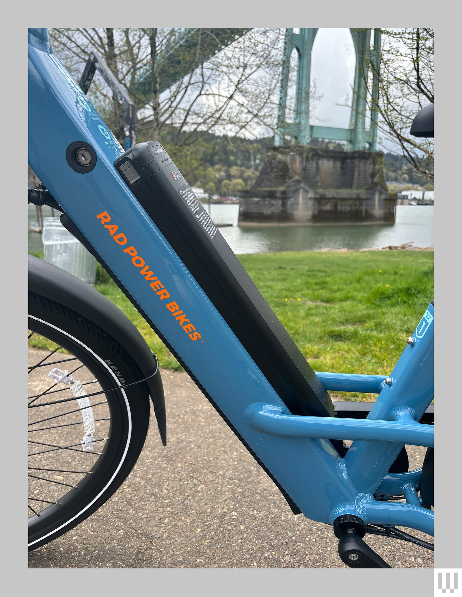 Close-up of the battery of a blue electric bike with the landscape of a park in the background