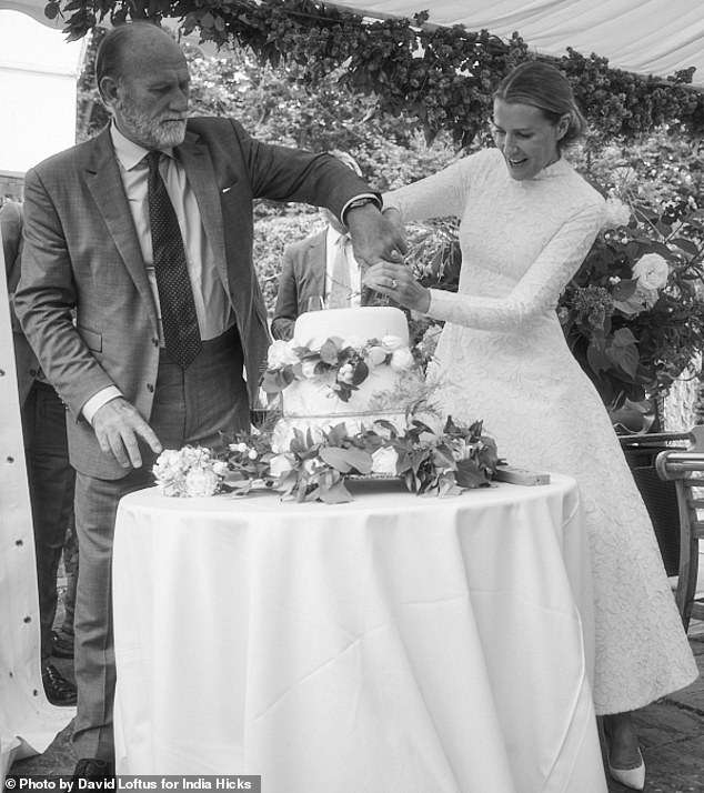 The couple cutting their three-tiered wedding cake decorated with white roses at their reception.