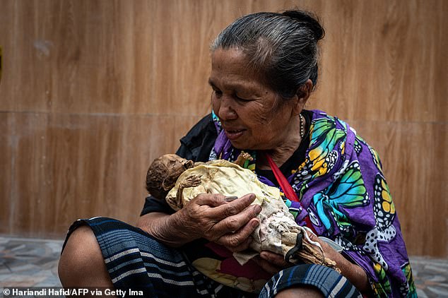 A member of the Toraja ethnic group holds the exhumed body of her baby, who died in 1988, during the traditional ritual known as Manene in Pangala, South Sulawesi, on August 27, 2024.