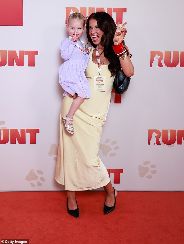 Amy Morgan looked elegant in a yellow dress as she playfully posed with her daughter in her arms on the red carpet.