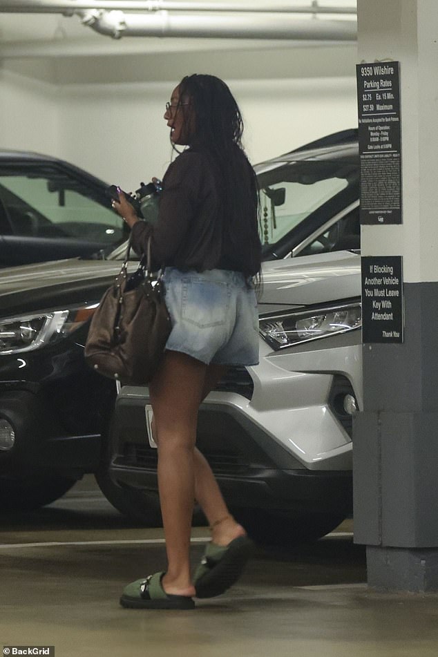 She accessorized her look with green slip-on shoes, a large brown handbag, square glasses, chunky rings, and a necklace with a striking circular pendant.