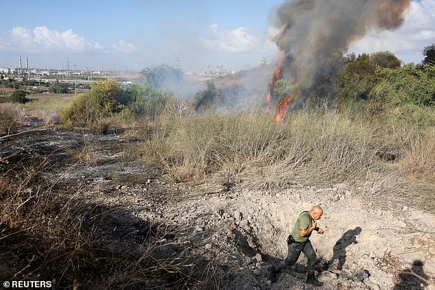 A man in a crater runs away as plumes of smoke rise and flames erupt behind him.