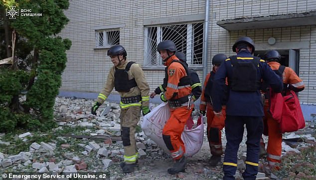 Emergency response crews carry a person wrapped in a blanket out of the building.