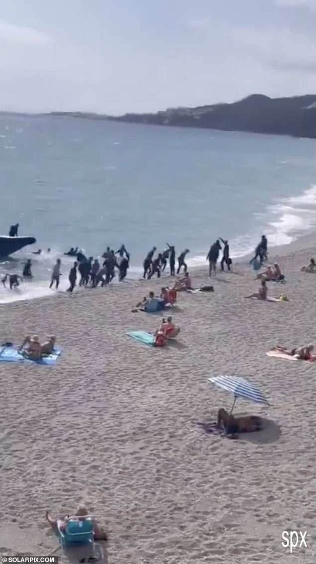 Shocked tourists sat on their deckchairs as the small boat approached the shore and the men disembarked before running or walking past them.