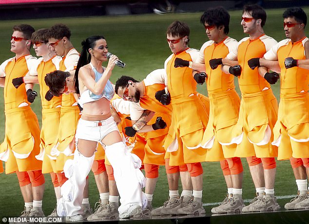 She was surrounded by a row of male dancers dressed in futuristic orange and white costumes.