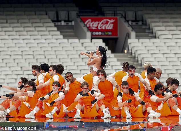 The dancers' outfits are tight-fitting, with geometric shapes and structured designs, complemented by red sunglasses, which give a sci-fi and avant-garde air.