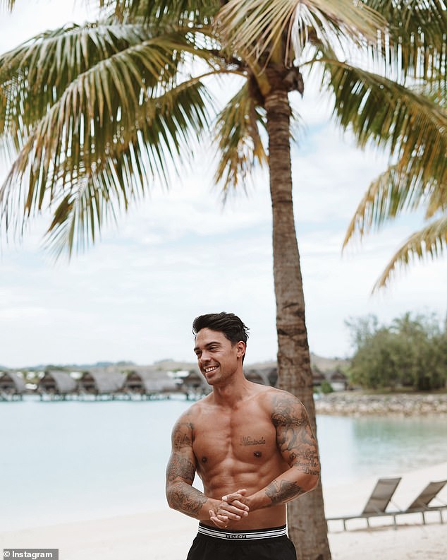 John was also photographed in a very relaxed pose on a wooden lounge chair on the beach before removing his shirt and flaunting his chiseled torso while standing in front of a palm tree.