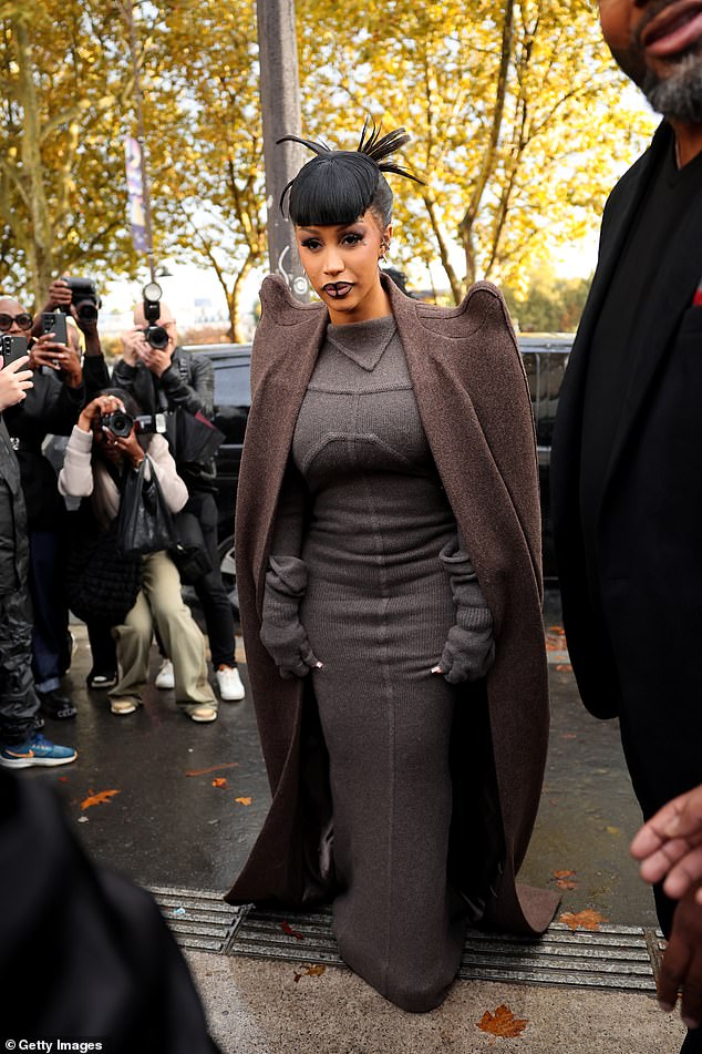 Cardi paired the elegant dress with a trendy brown trench coat, which featured dramatic curved shoulder pads.