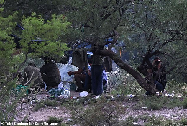 Here you can see a human smuggler using binoculars to spy on DailyMail.com during a trip to report on holes in the border wall.