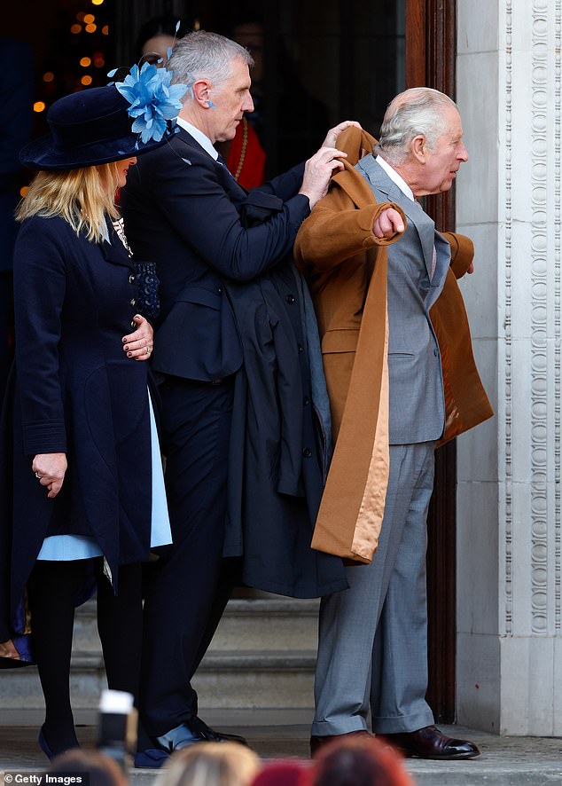 King Charles III's police protection officer helps him into his coat after a visit to Luton Town Hall, December 2022.