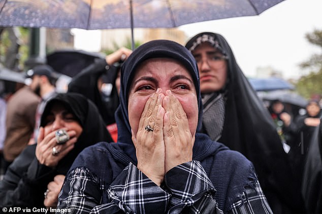 A woman reacts while standing in the rain with other protesters during an anti-Israel protest in Tehran's Palestine Square on September 28, 2024, after the Iranian-backed Lebanese group Hezbollah confirmed reports of the assassination of its leader Hassan Nasrallah on an Israeli plane. strike in Beirut the day before