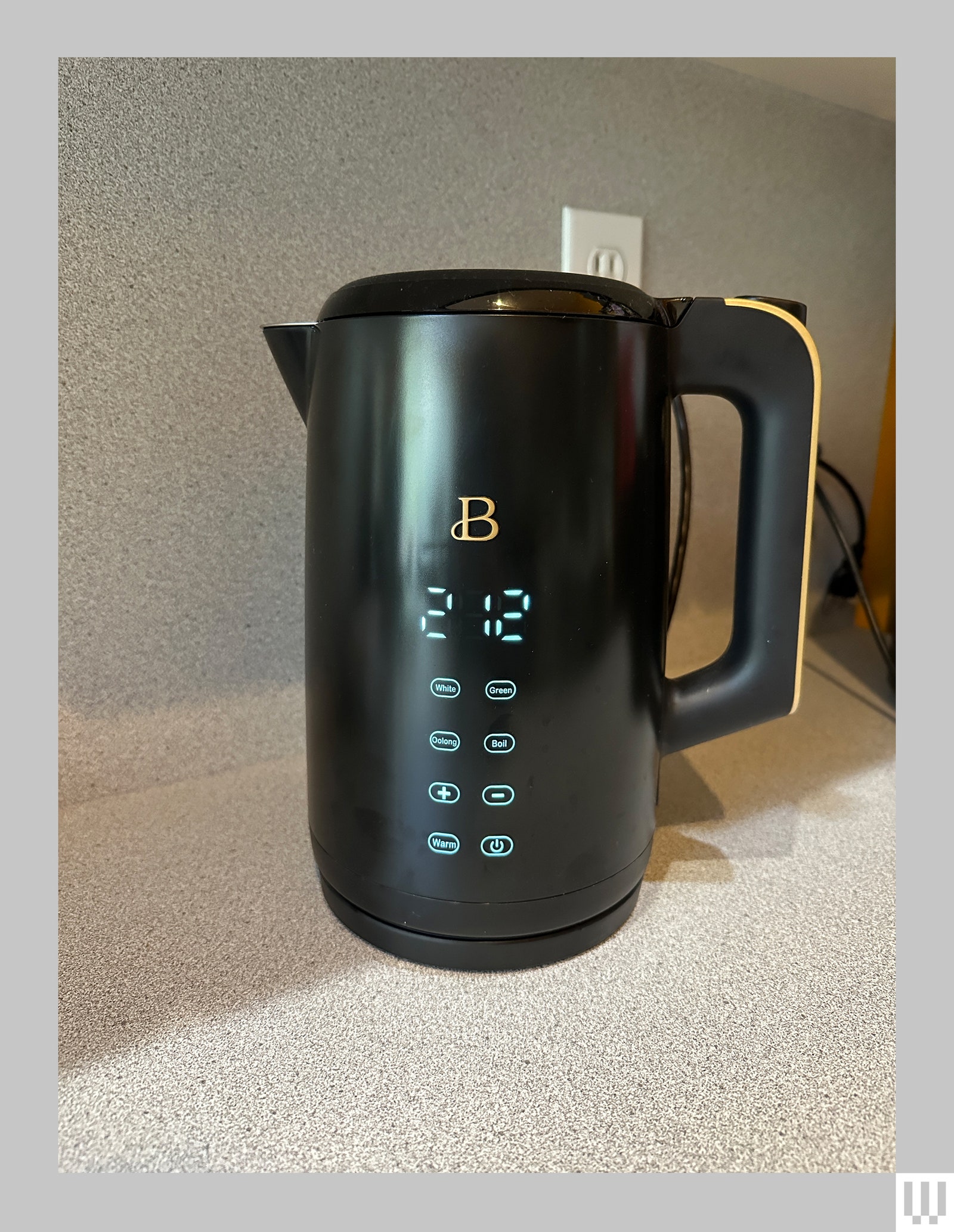 Black cylindrical kettle with digital display and flat buttons on a mottled countertop