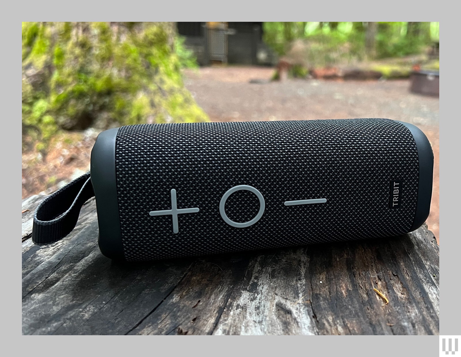 Black cylindrical portable speaker placed horizontally on a wooden picnic table in the forest