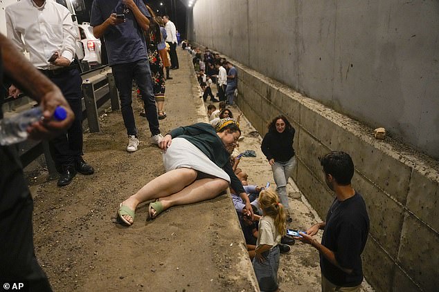 People take shelter on the side of a road as a siren sounds warning of incoming missiles fired from Iran on a highway in Shoresh, between Jerusalem and Tel Aviv in Israel, Tuesday, October 1, 2024.