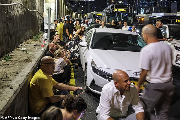 People take shelter behind vehicles under a roadside bridge in Tel Aviv on October 1.