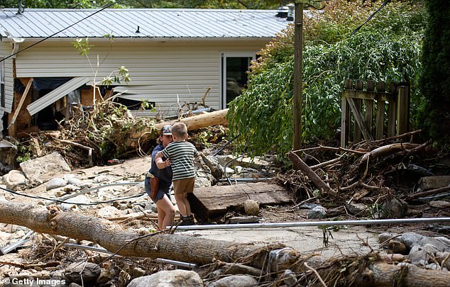 Leo Grindstaff, 12, left, helps his brother Gabe, 4, as he walks to his grandparents' house to help rescue items after Hurricane Helene.