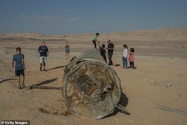 People take pictures and stand on the remains of a missile in Arad, Israel.