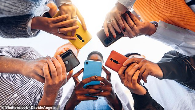 Teenagers gather in a circle in front of their phones. Growing up surrounded by technology has damaged attention span (file image)