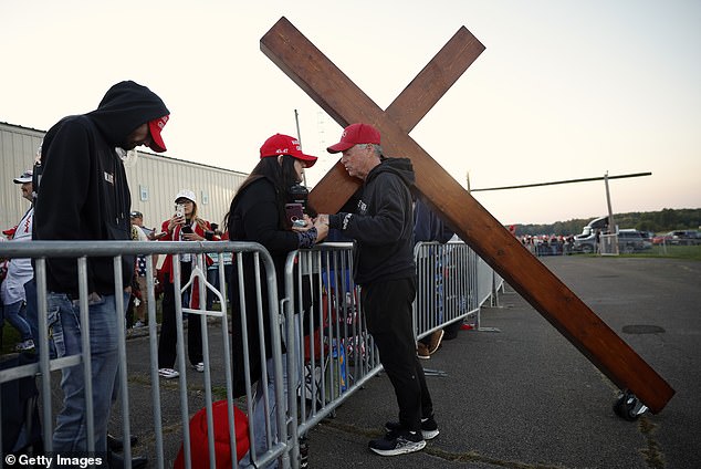 Don Deazley carries a cross as he prays with Sue Hensal and others as they wait in line for a rally for Republican presidential candidate, former United States President Donald Trump, at the Butler Farm Show Inc. on October 5, 2024 in Butler, Pennsylvania.