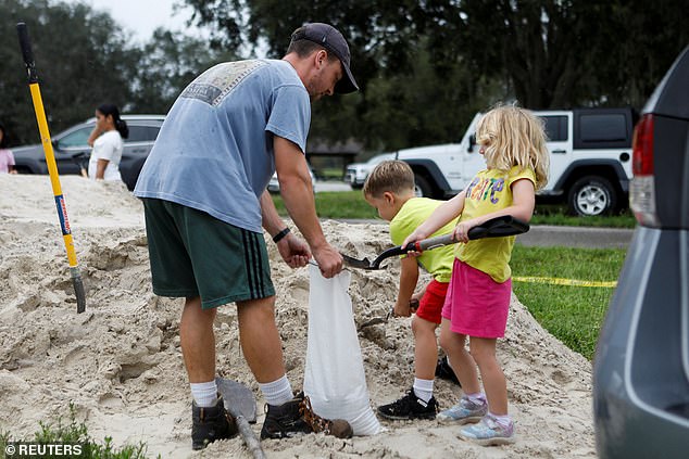 Tom Murphy prepares a sandbag with children, as sandbags are distributed to Pinellas County residents ahead of the expected arrival of Tropical Storm Milton, in Seminole, Florida, on Sunday.