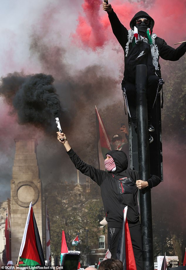 Pro-Palestinian protesters hold smoke flares as they cling to a traffic light outside Downing Street.