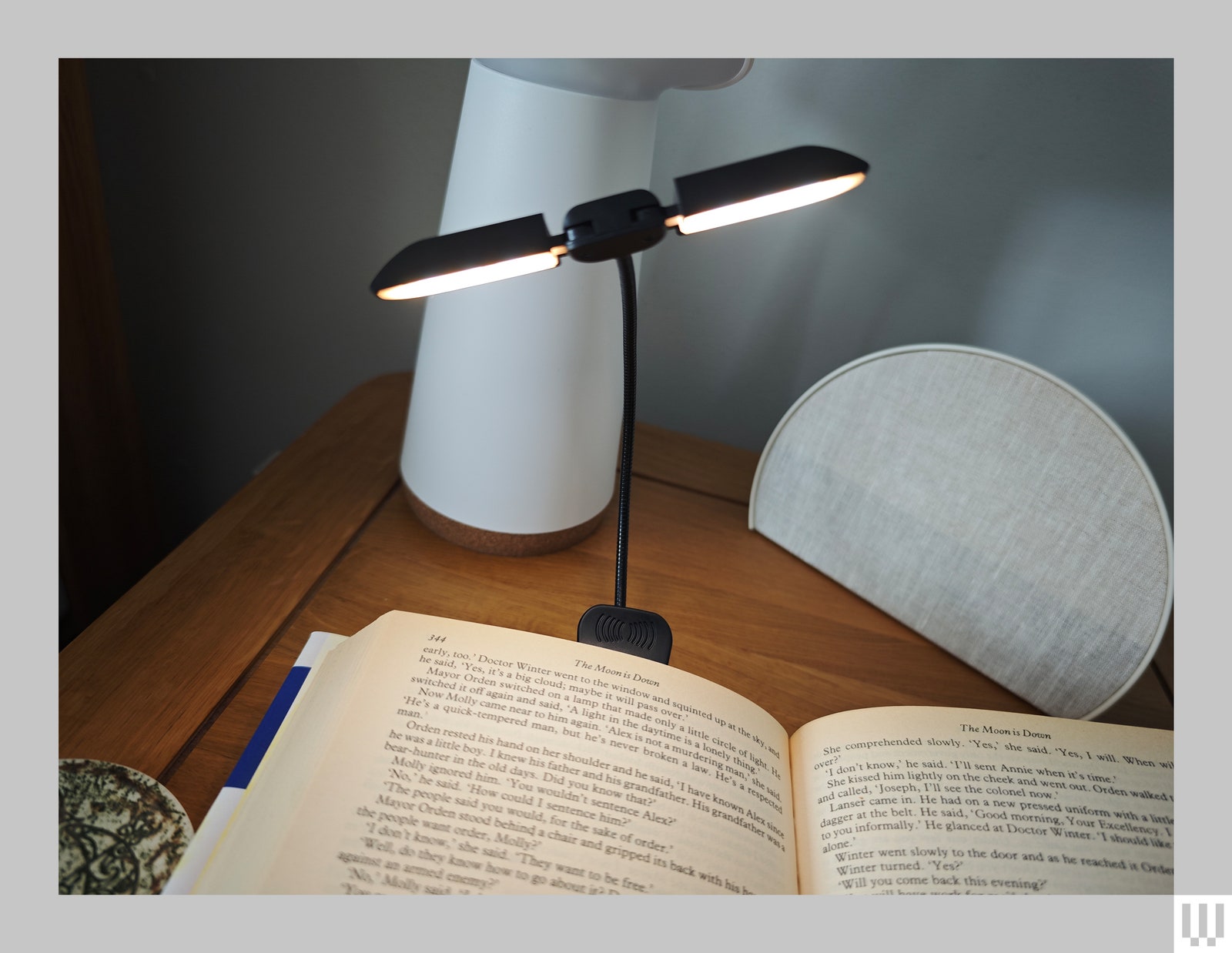 An open book on a wooden nightstand with a thin double-sided light attached to the book