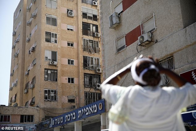 A person reacts to the site where a rocket, launched from Lebanon, damaged a residential apartment building when it landed in Israel