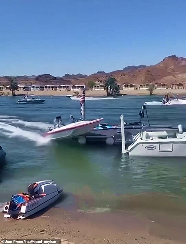 The boat, piloted by an elderly man with a woman sitting on the passenger side, bounces off a buoy before hitting the shore, causing the boat to come to an abrupt stop.