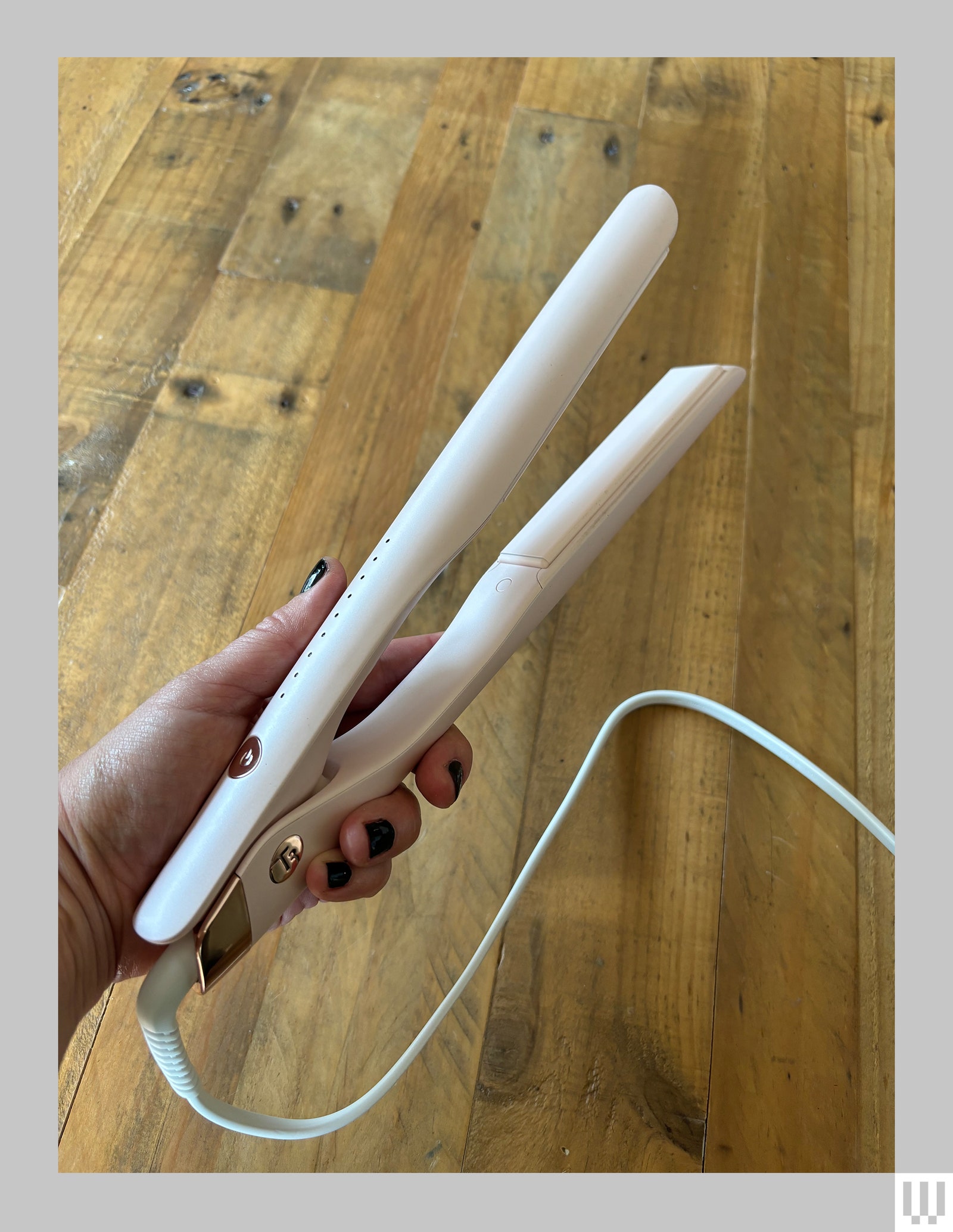 Hand holding a thin white hair straightener showing a pearl colored panel on the inside of one of the clamps.