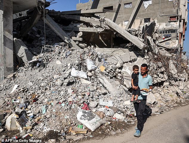 A man carries a child as he walks past a collapsed building in the Bureij camp for Palestinian refugees in the central Gaza Strip on October 9.