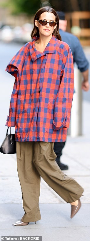 Wearing an oversized red and blue checked jacket, while carrying a small handbag.