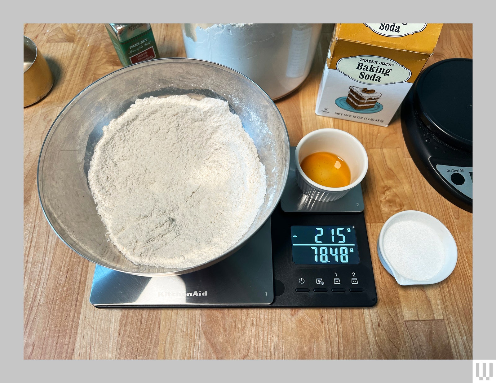 Large black and silver digital scale with a metal container with flour and an additional container on top, on a kitchen...