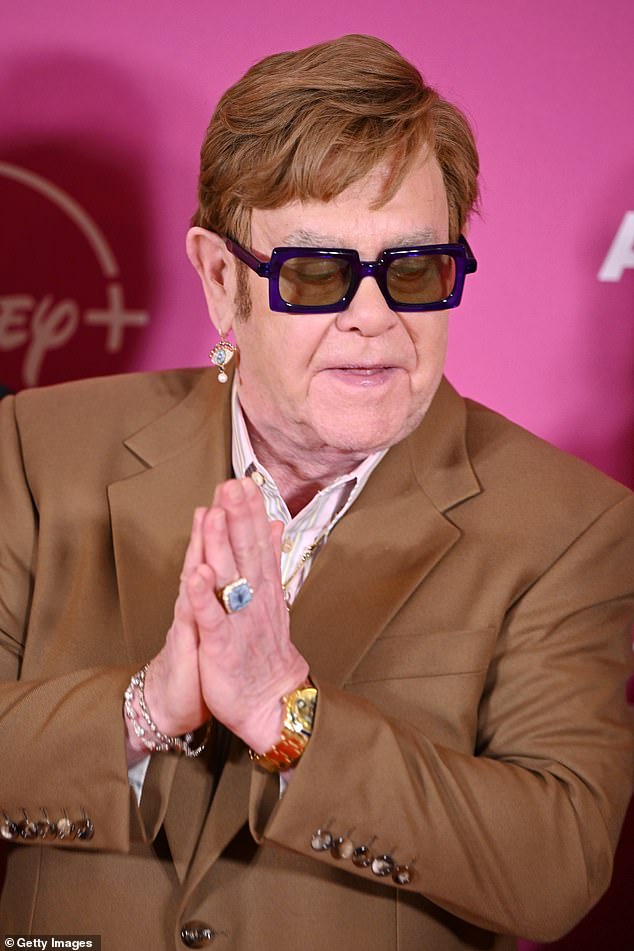 Elton looked as fashionable as ever with his trademark glasses and wore a dark brown suit with a pink striped shirt.