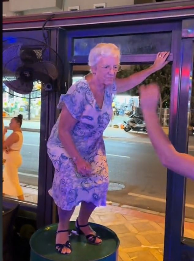 Wearing a loose floral dress and practical black sandals, the fun-loving retiree clings to the steakhouse window frame.