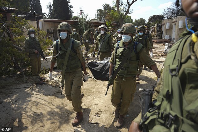 Israeli soldiers carry the body of a person killed in the Hamas attack on the Kfar Azza kibbutz on Tuesday, October 10, 2023.